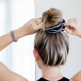 Person styling hair with a scrunchie against a white background. Retailer sustainable plastic-free hair accessories B2B #color_tuxedo